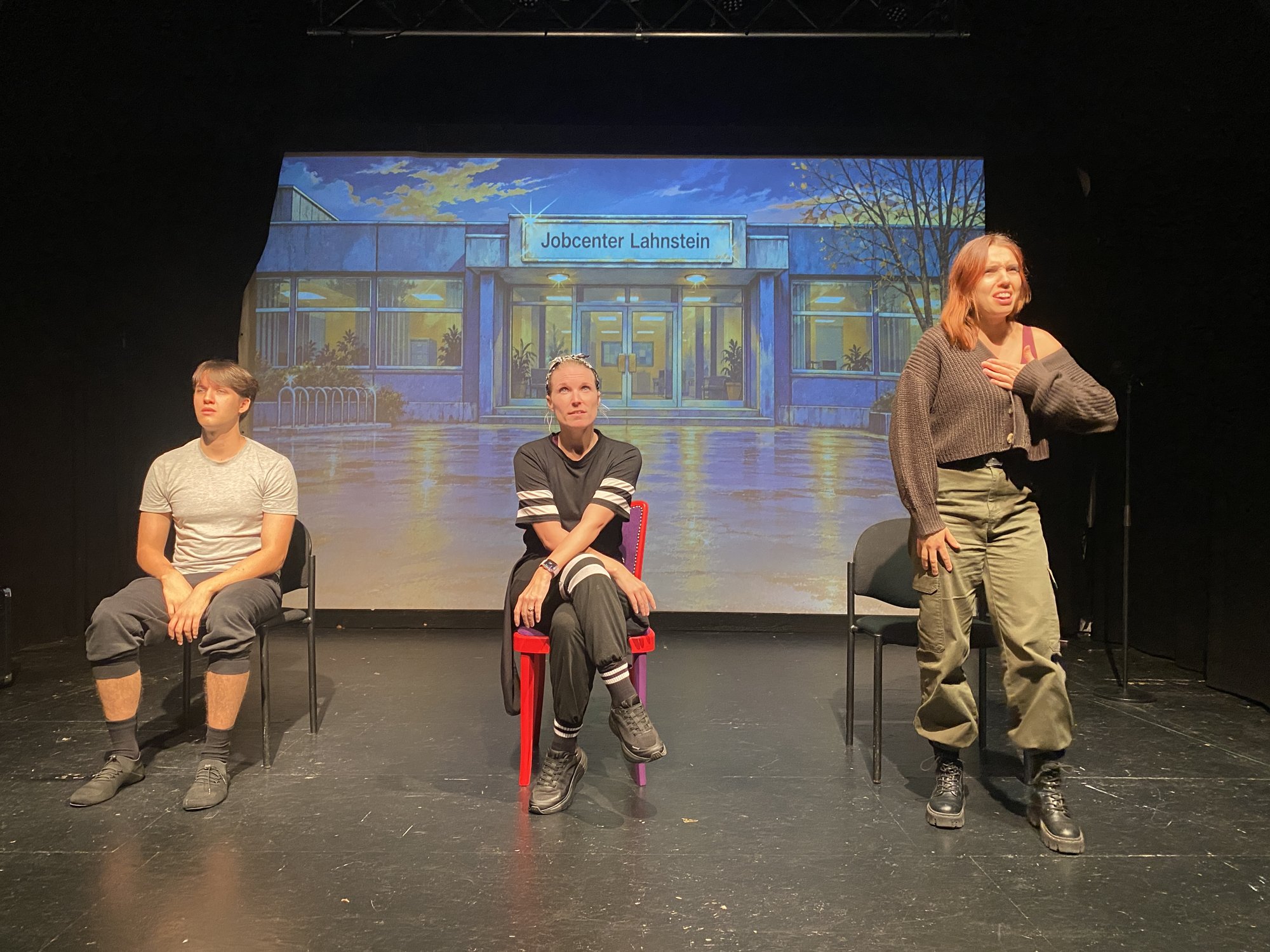 Ensemble probt eine Szene vor dem Jobcenter-Bühnenbild im Theater Lahnstein